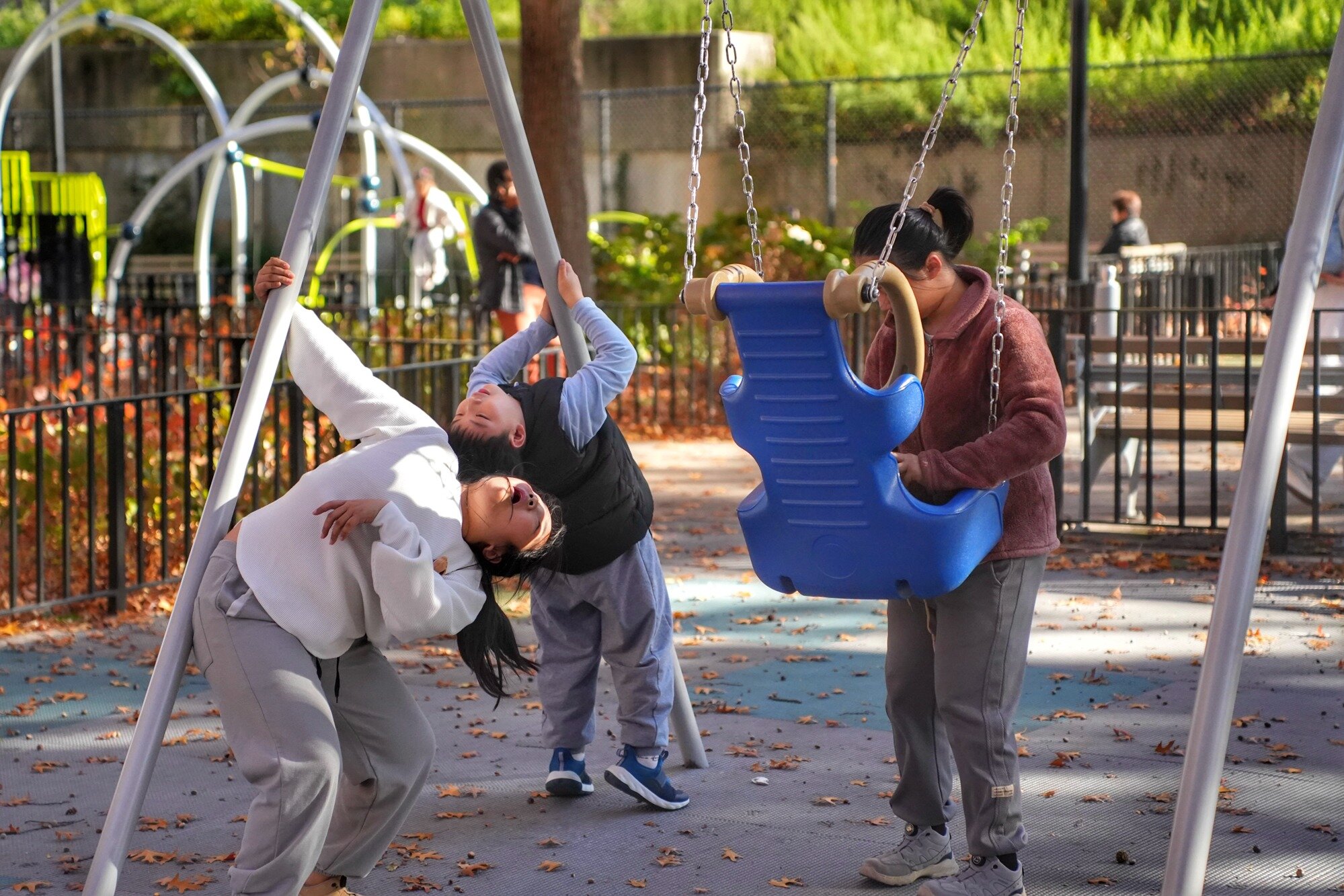 A woman and two children share a swing on a mild autumn afternoon. Nov. 8, 2025.