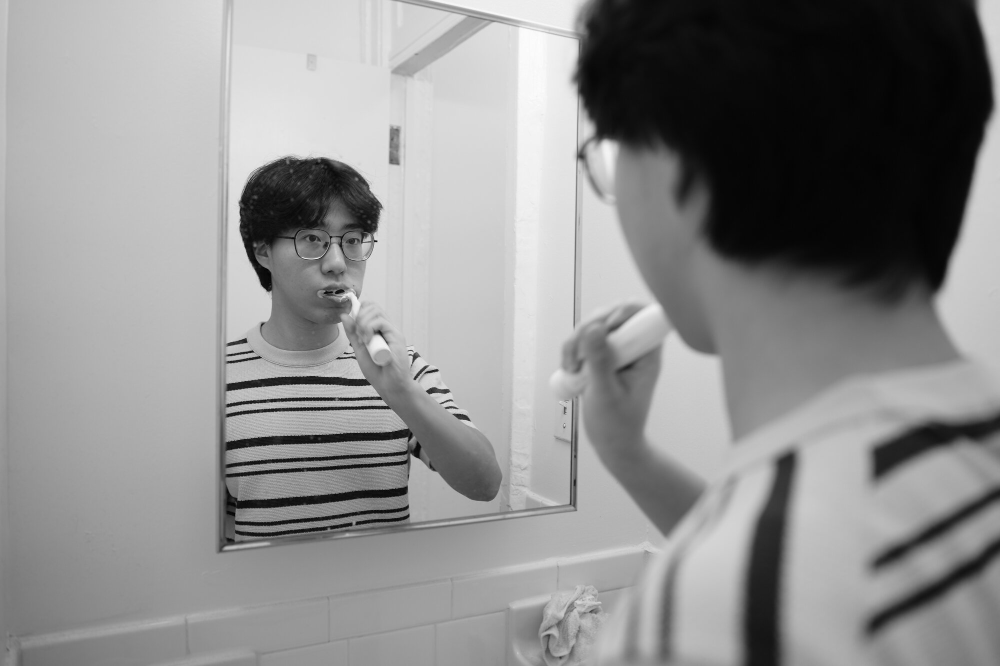 Ziyuan Yin, 23, brushes his teeth at home, reflected in the bathroom mirror. Nov. 19, 2025.